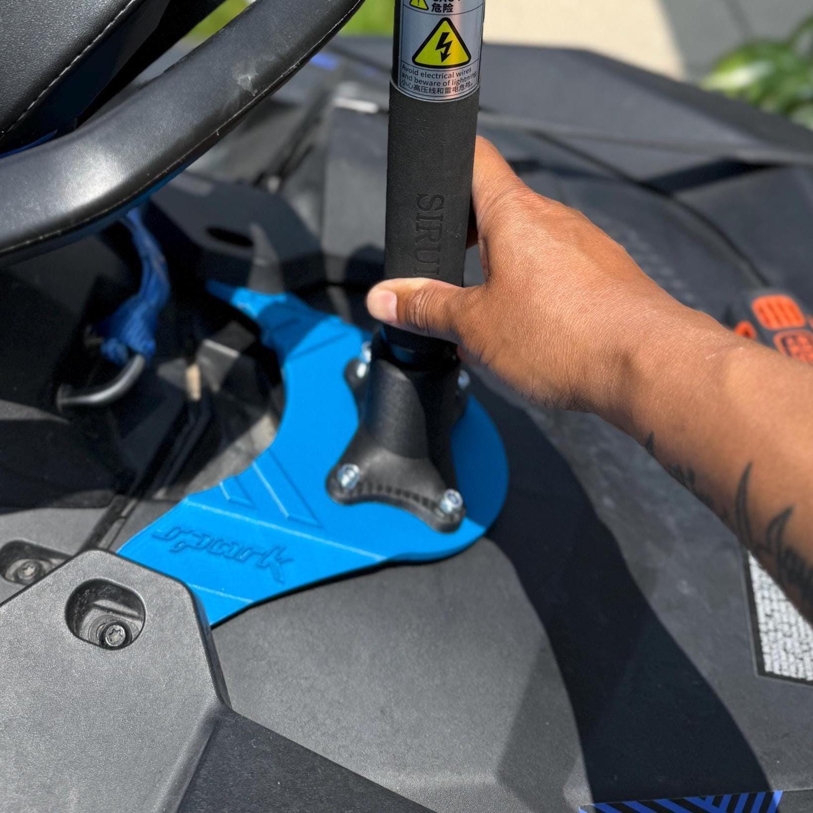 Close-up of a hand fitting a camera pole into the black mount bolted to the Sea-Doo's rear, blue base plate visible