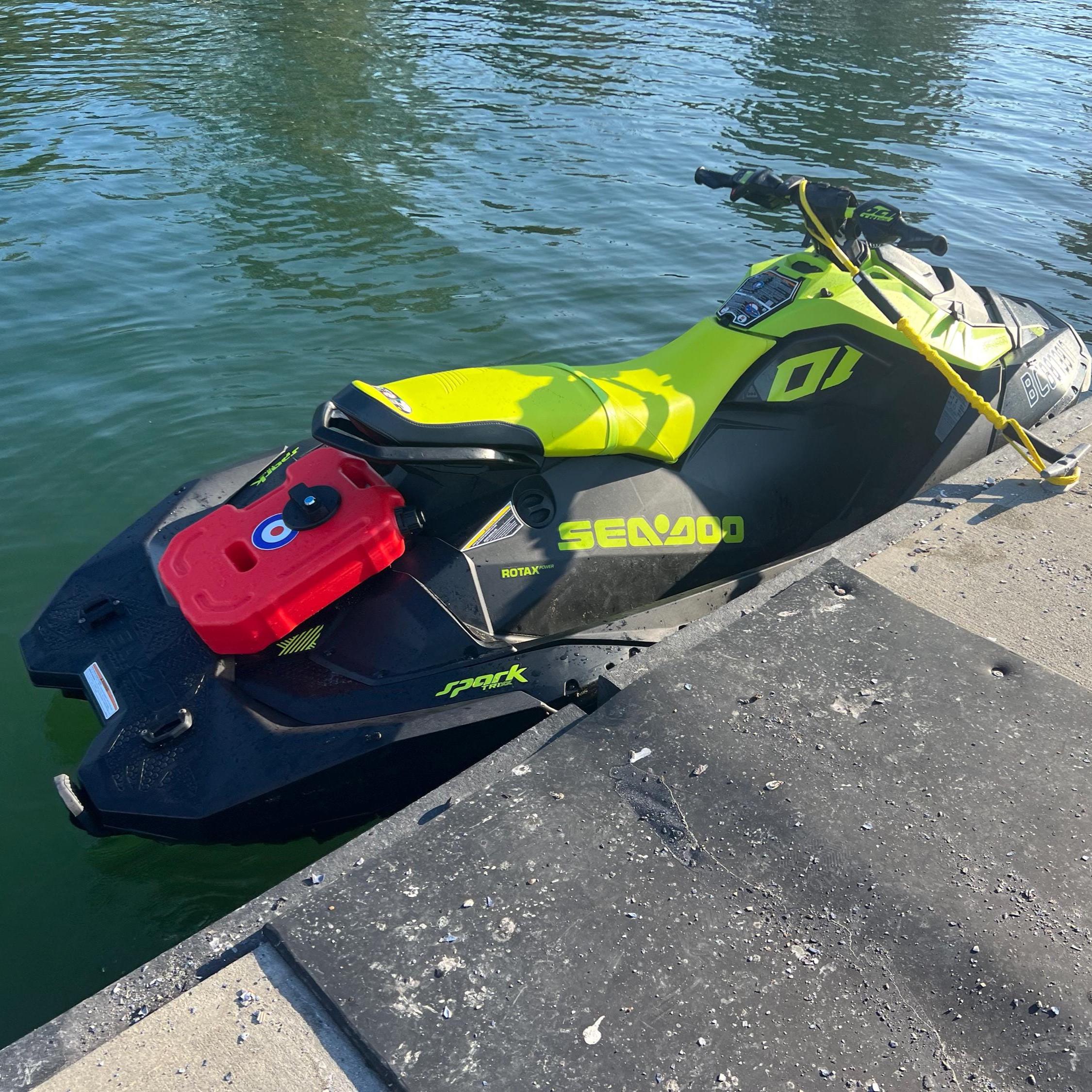Green Sea-Doo Spark Trixx docked on the water with a red fuel can mounted on the back