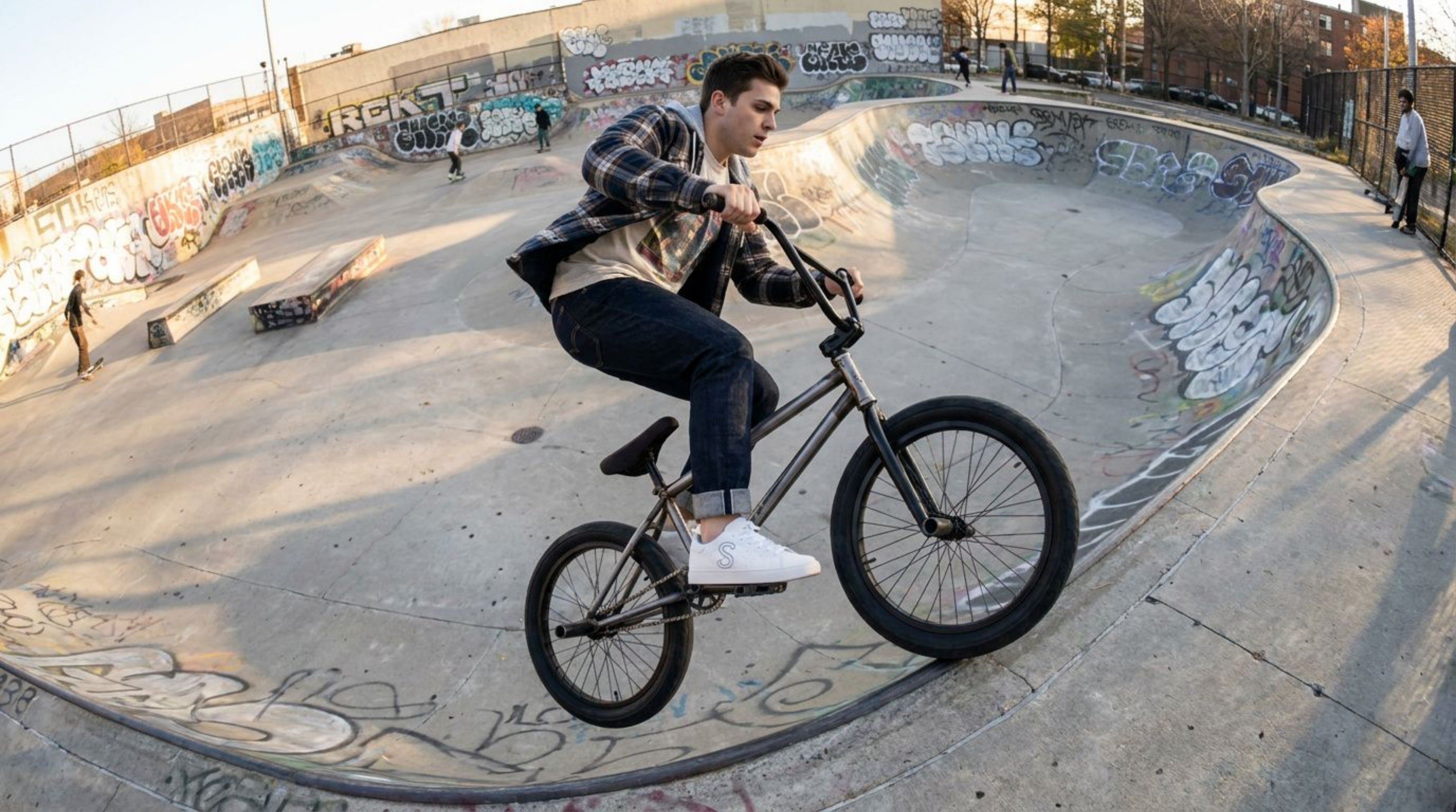 Man riding a BMX bike wearing the white sneakers at a graffiti-covered skate park