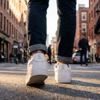 Close-up of white sneakers on a person's feet with rolled jeans, walking on a city street