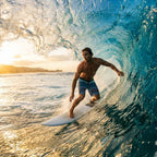 A surfer riding inside a breaking wave at sunset, wearing striped board shorts