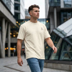 Man wearing cream SparkyCA logo tee and jeans, walking through a city plaza