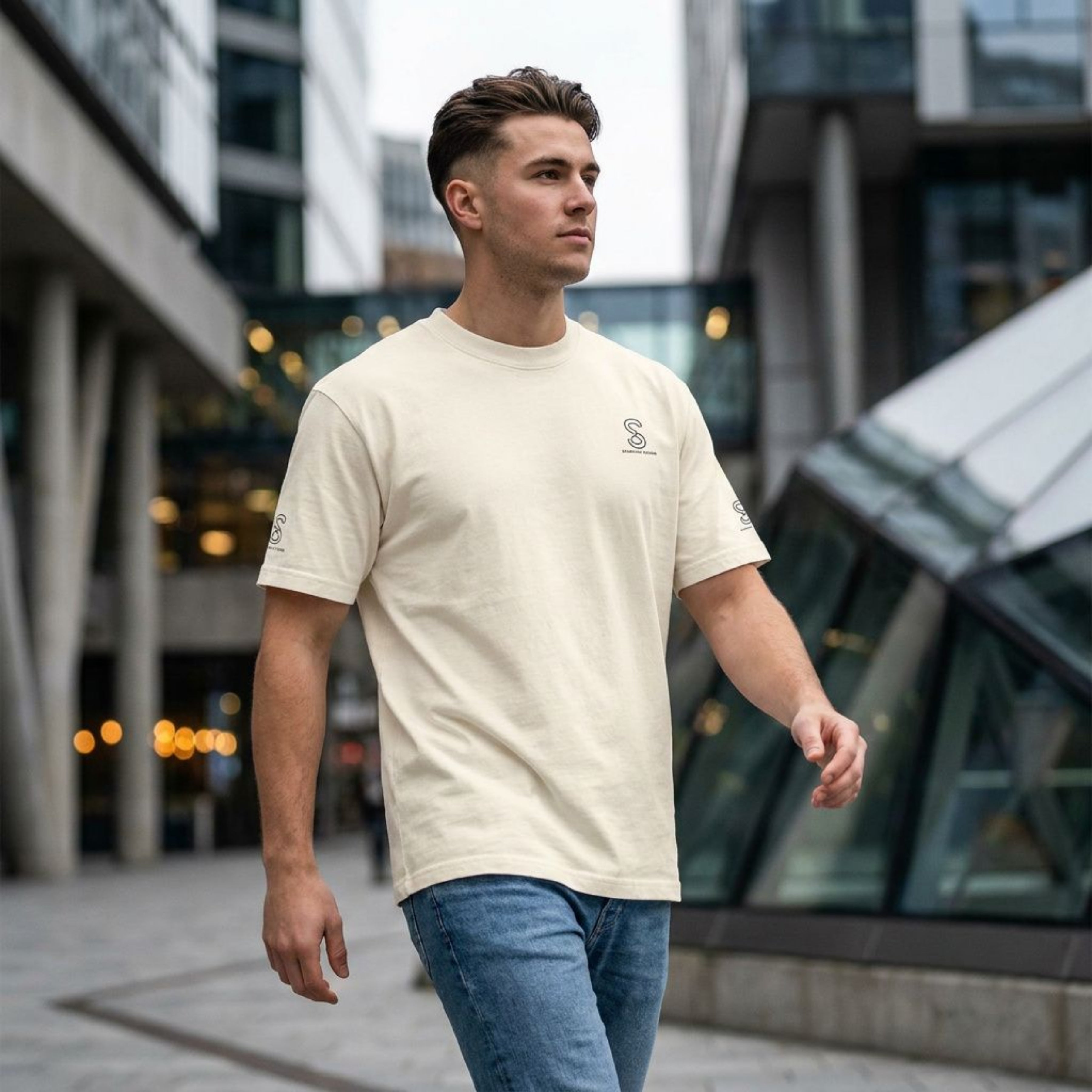 Man wearing cream SparkyCA logo tee and jeans, walking through a city plaza