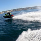 Rider on a green Sea-Doo Spark carving through water near coastal cliffs with a red fuel can mounted on back