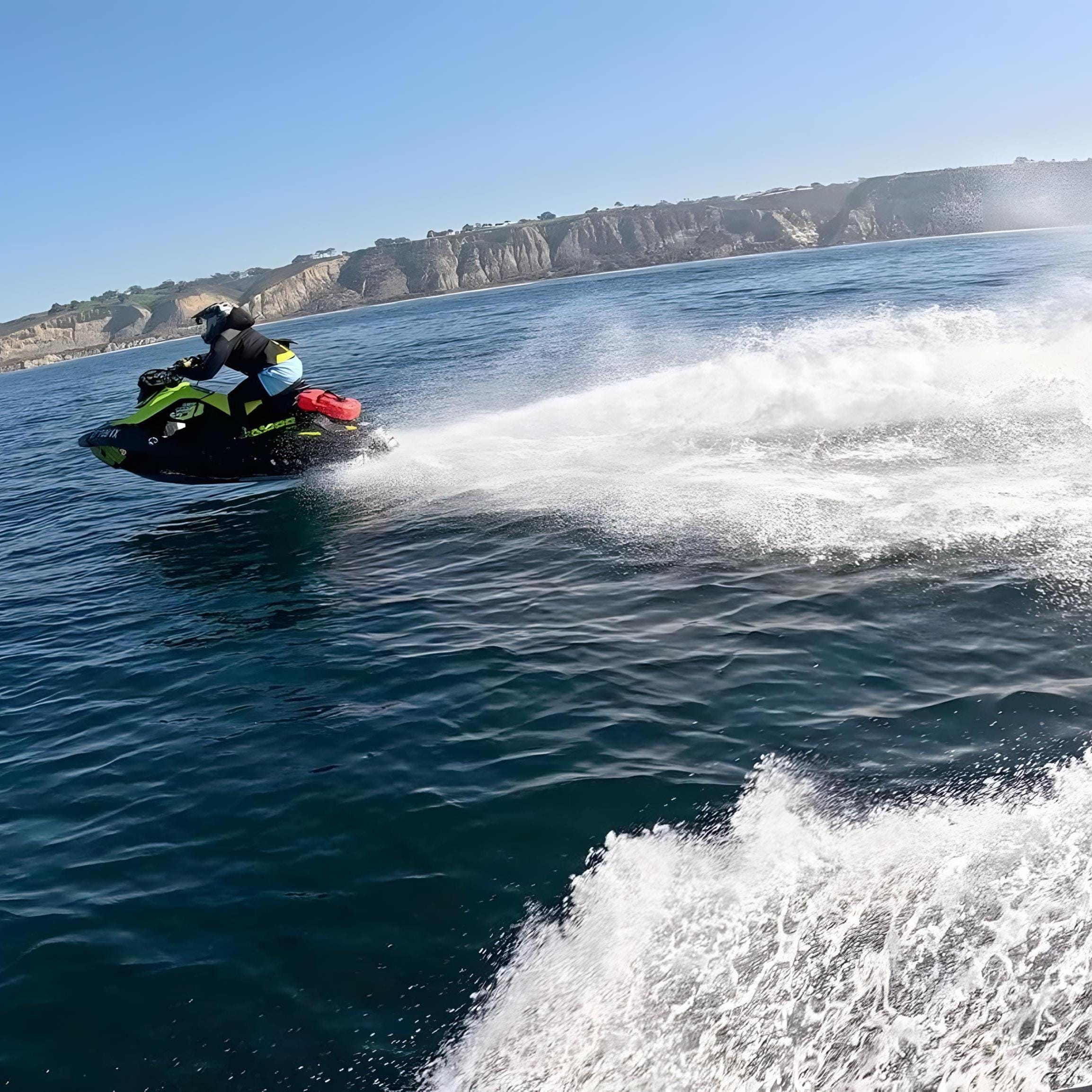Rider on a green Sea-Doo Spark carving through water near coastal cliffs with a red fuel can mounted on back