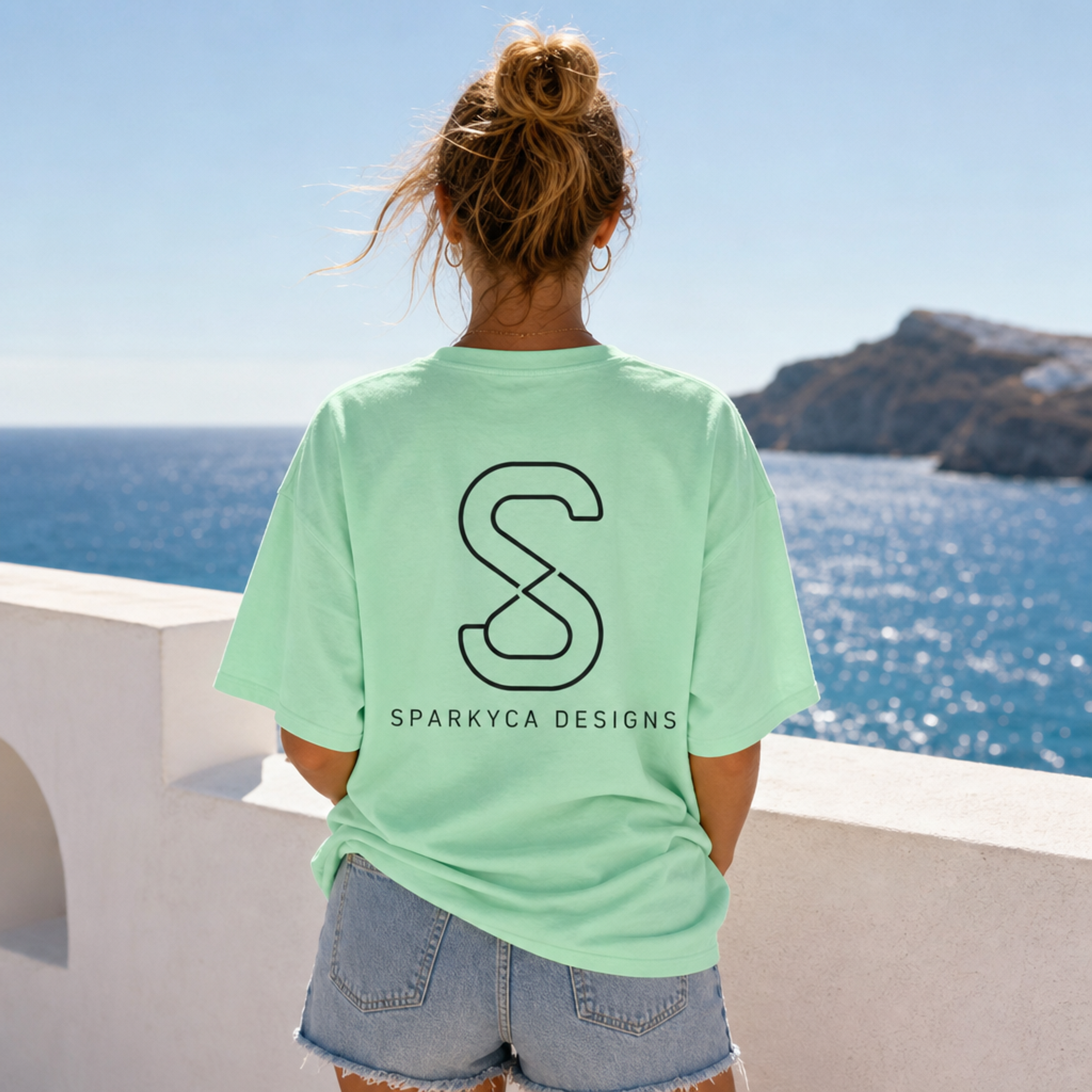 Woman wearing the SparkyCA Logo Tee in Safety Green, back view showing the S logo print, oceanside lifestyle photo