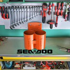 Orange Sea-Doo Spark Trixx cup holder displayed on a workbench with tools