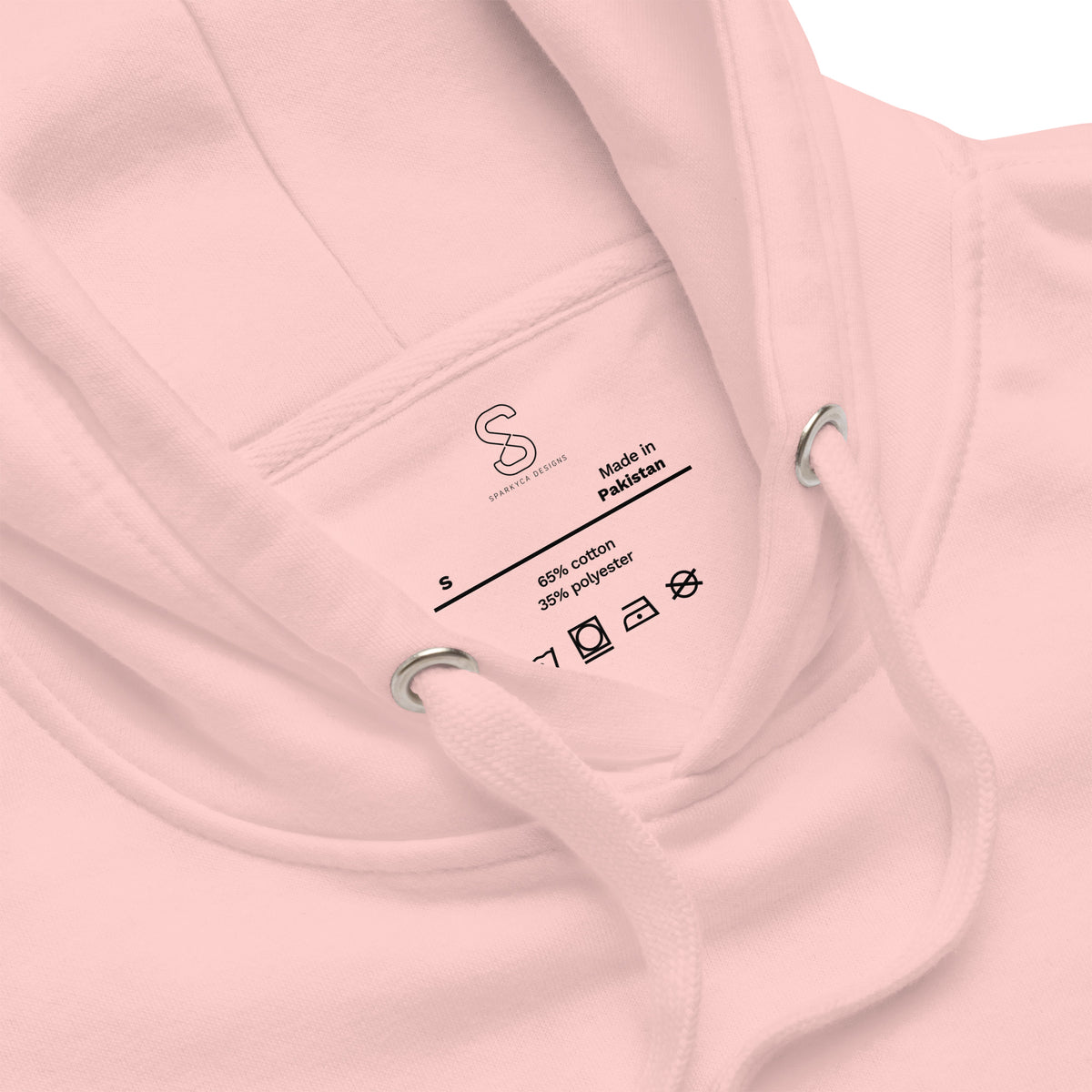 Close-up of the Light Pink hoodie's inner neck label showing the SparkyCA Designs logo, size, and made-in-Pakistan fabric tag